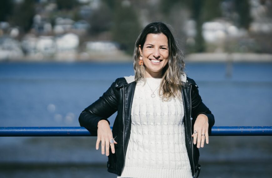 Mulher apoiada em uma cerca de madeira vestindo jaqueta de couro com um lago ao fundo